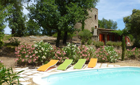 The swimming pool viewed from the garden. There are 4 brightly coloured sun loungers and the Moulin is in the background. The pool is bordered with Oleanders.